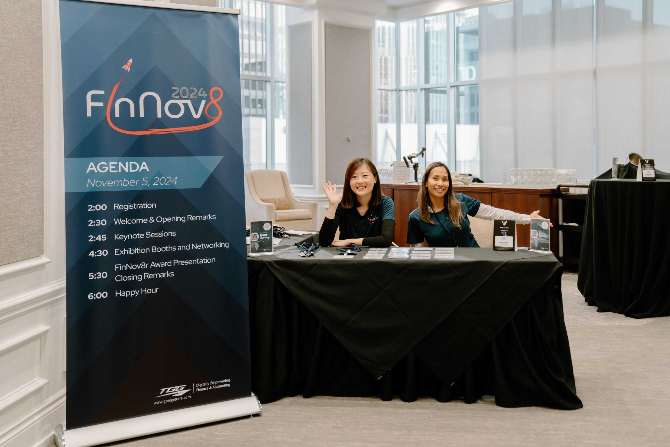 FinNov8 2024 fintech conference event photography showing two smiling staff at registration desk with event agenda banner at Toronto corporate conference by Origin Films
