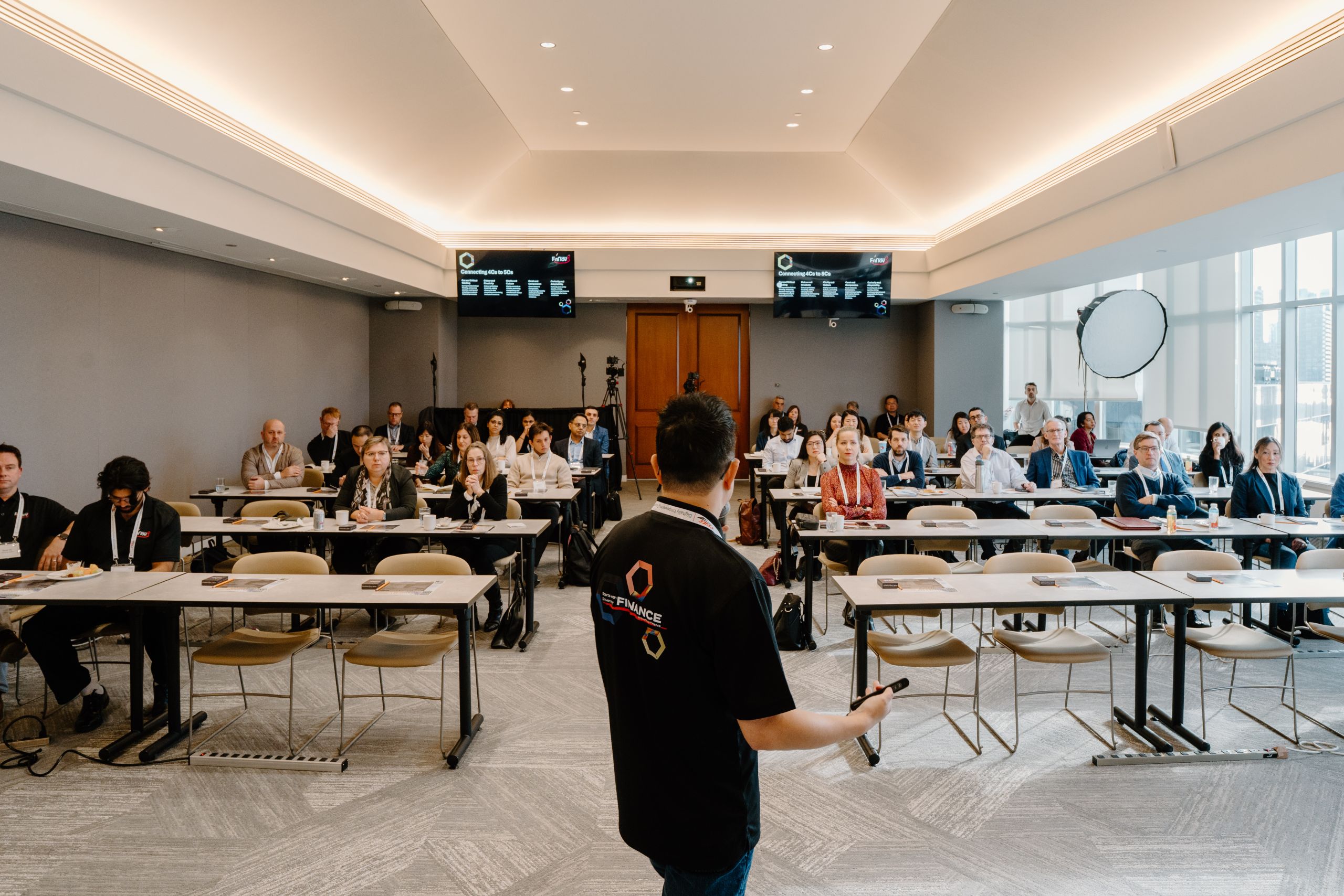 Finance conference speaker in branded t-shirt presenting to a large seated audience at a corporate fintech event in Toronto photographed by Origin Films professional event photography